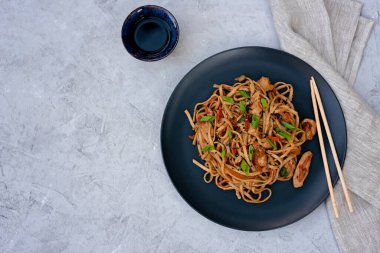 Tavuk sebzeli Asya udonu erişte ve çubuklu teriyaki sosu ve gri beton arka planda keten peçete. Çin ve Japon mutfağı. Boşluğu kopyala.