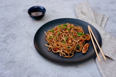 Tavuk sebzeli Asya udonu erişte ve çubuklu teriyaki sosu ve gri beton arka planda keten peçete. Çin ve Japon mutfağı.