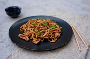Tavuk sebzeli Asya udonu erişte ve çubuklu teriyaki sosu ve gri beton arka planda keten peçete. Çin ve Japon mutfağı.
