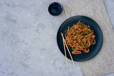 Tavuk sebzeli Asya udonu erişte ve çubuklu teriyaki sosu ve gri beton arka planda keten peçete. Çin ve Japon mutfağı. Boşluğu kopyala.