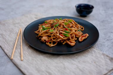 Tavuk sebzeli Asya udonu erişte ve çubuklu teriyaki sosu ve gri beton arka planda keten peçete. Çin ve Japon mutfağı.