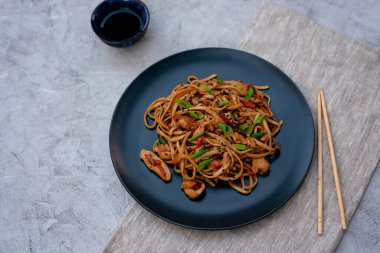 Tavuk sebzeli Asya udonu erişte ve çubuklu teriyaki sosu ve gri beton arka planda keten peçete. Çin ve Japon mutfağı.