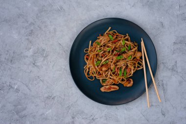 Tavuk sebzeli Asya udonu erişte ve gri beton arka planda çubuklarla teriyaki sosu. Çin ve Japon mutfağı. Boşluğu kopyala.