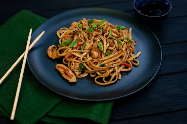 Tavuk sebzeli Asya udonu erişte ve çubuklu teriyaki sosu ve siyah ahşap arka planda yeşil peçete. Çin ve Japon mutfağı.