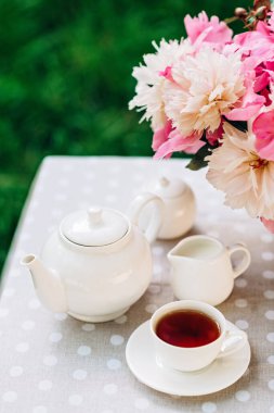 Açık havada samimi romantik bir kahvaltı. Şakayık çiçeği vazosu, çaydanlık ve çay masanın üstünde. Anneler günü ya da kadınlar günü için tebrikler. Yumuşak seçici odak.