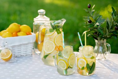 Limonata tazeleyici bir içecek ve limonlu kavanozlar, taze nane ve limon ve kumkatlı bir sepet buz. Yaz pikniği. Yumuşak seçici odak.