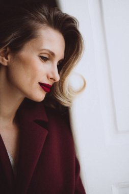 Güzel seksi bir kızın portresi bukleli ve parlak dolgun dudaklı kırmızı rujlu bordo ceketli. Güzellik ve moda. Yumuşak seçici odak.