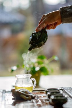 Çin çay seremonisi. Ellerindeki seramik çaydanlık buharlı ünlü Çin beyaz bardaklarına dökülüyor. Yumuşak odak.