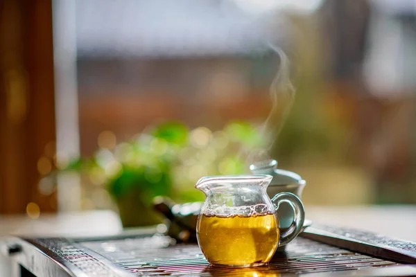 Hot green tea with steam in a transparent teapot against the background of a window. Tea ceremony.