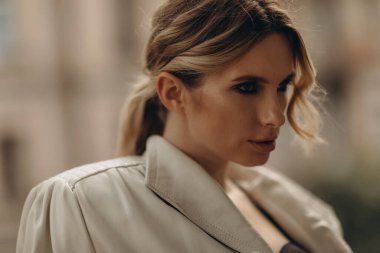 Zarif, zarif, bej renkli bir kadının şık bir portresi. Deri palto ve açık havada dumanlı göz makyajı. Bahar - sonbahar moda konsepti. Yumuşak seçici odak.