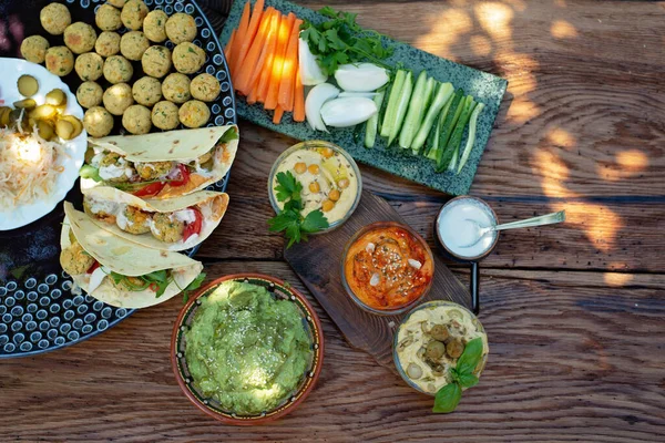 Tahta meşe masasında vejetaryen pikniği, humus, falafel, pita, sebze, ıspanak, fesleğen ve ayçiçeği tohumu pesto sosu. Sağlıklı Akdeniz yemekleri.