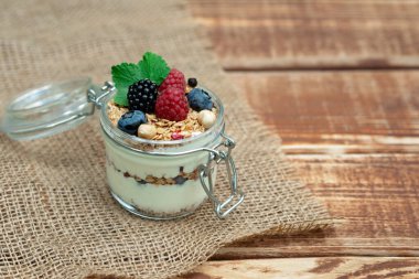 Yoğurtlu müsli granola ve taze ahududu, yabanmersini ve böğürtlen, ahşap arka planda cam bir kavanozda fındık. Sağlıklı ve sağlıklı kahvaltı..