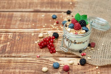 Yoğurtlu müsli granola ve taze üzümlü üzümlü ahududu ve böğürtlen, ahşap arka planda cam bir kavanozda fındık. Sağlıklı kahvaltı..