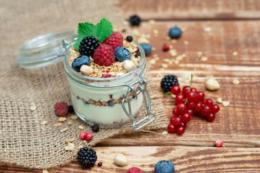 Yoğurtlu müsli granola ve taze üzümlü üzümlü ahududu ve böğürtlen, ahşap arka planda cam bir kavanozda fındık. Sağlıklı kahvaltı..