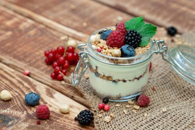 Yoğurtlu müsli granola ve taze üzümlü üzümlü ahududu ve böğürtlen, ahşap arka planda cam bir kavanozda fındık. Sağlıklı kahvaltı..