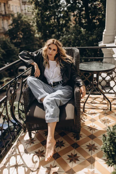 Şık, şık, göz makyajlı, kot pantolonlu, beyaz tişörtlü ve koltukta siyah deri ceketli bir kadın. Bahar sonbahar moda konsepti. Yumuşak seçici odak.
