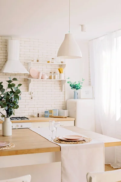 Modern interior of a white light kitchen in a Scandinavian style, a wooden table, natural textiles, a brick wall and kitchen utensils. Light loft. Soft selective focus.