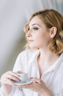 Aydınlık bir odada açık renk gömlekli güzel sarışın kız işe gitmeden önce bir fincan kahvenin tadını çıkarıyor. Banyodaki gizli elbiseli kız..