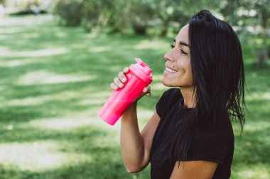 Bronz tenli genç bayan sporcu, açık hava eğitiminden sonra protein içeceği içiyor. Spor beslenmesi. Yumuşak seçici odak.