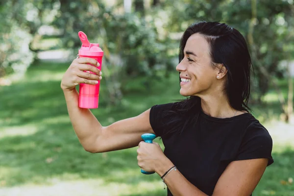 Bronz tenli genç bayan sporcu, açık hava eğitiminden sonra protein içeceği içiyor. Spor beslenmesi. Yumuşak seçici odak.