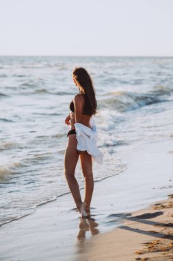 Siyah bikinili, beyaz tişörtlü, kumsalda bronzlaşmış vücutlu, ince, güzel bir kadın. Yumuşak seçici odak, sanat burnu.