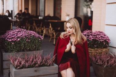 Burgundy Marsala 'da, içinde kasımpatı olan bir kafenin merdivenlerinde şık bir sonbahar kıyafeti giymiş güzel sarışın bir kadın. Yumuşak seçici odaklanma. Sanatsal gürültü.