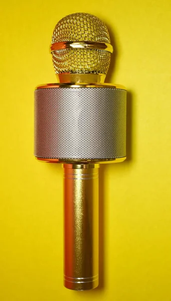 Sarı arka planda, dikey olarak yerleştirilmiş, altın metal karaoke mikrofon.