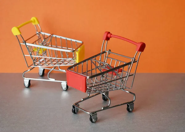Gri-turuncu arka planda iki boş süpermarket arabası.