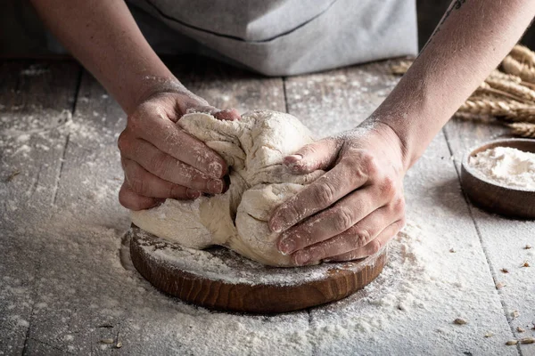 baker's hands make dough on old wooden background with flour