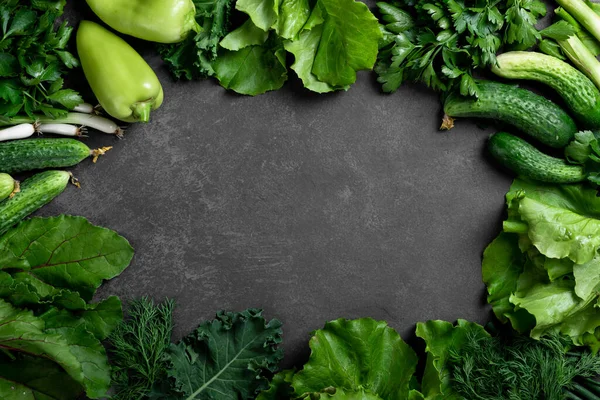 green vegetables and herbs on a dark stone background, top view, place for text