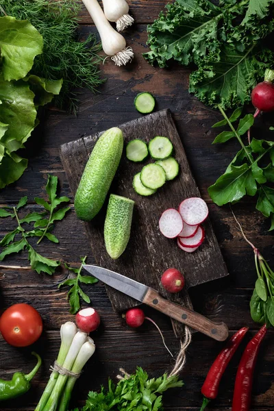 different farm vegetables and herbs on a dark wooden background, top view