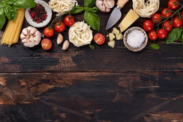 italian food ingredients background. Spaghetti, tagliatelle pasta, basil, parmesan, tomatoes, garlic on an old rustic wooden table, top view, copy space