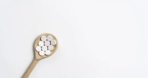 Träsked med tabletter på vit bakgrund — Stockfoto