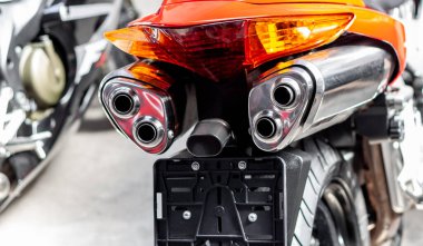 Egzoz boruları ve turuncu motosiklet fren lambaları yakın çekim. Garajdaki spor bisikletinin sesi. Arka manzara, klasik yol bisikleti tekerleği. Bir çift krom boru seçici odak noktası. Plakanın altına yerleştir