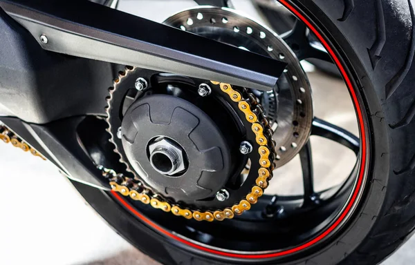 Rear wheel of a sports motorcycle with red-black cast disc, close-up. Running gear, chain, sprocket, motorcycle tire, brake discs. Road fast motorcycle in the garage for repair, maintenance.