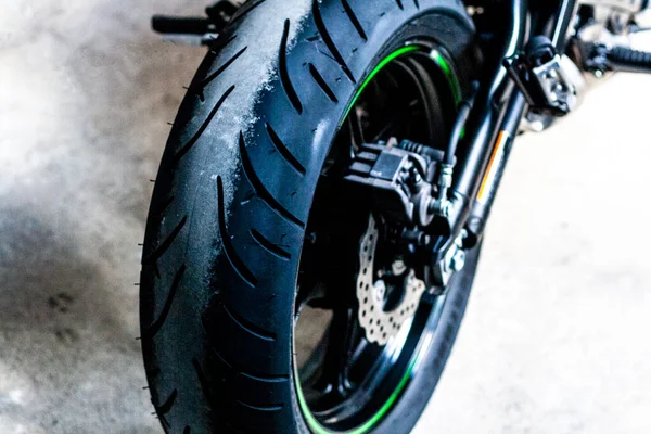 緑とスポーツバイクの後輪黒のキャストディスク クローズアップ 走行ギア サスペンション オートバイタイヤ ブレーキディスク サポート 道路修理 メンテナンスのためのガレージで高速オートバイ — ストック写真