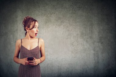 Hareket eden telefon tutarak ve duvar arka plan üzerinde izole kopya alanı uzağa bakarak sürpriz genç bir kadın portresi