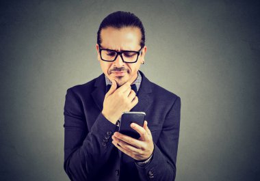 Gri arka plan üzerinde cep telefonu kullanırken çapraşık ve şüpheci seyir gözlük iş adamı. 