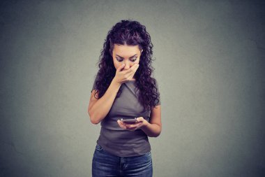 Genç kız ağız kapsayan ve gri arka plan üzerinde güçlü tepki Smartphone cep telefonu ile haber okumak hayrete düşürdü.. 