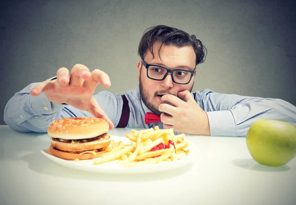 健康な青リンゴの代わりにフライド ポテトとチーズバーガーのための欲求を持つメガネの若い肥満の人 — ストック写真