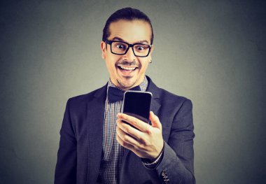 Smartphone kullanarak ve iyi haber alma mutlu hayret seyir gözlüklü zarif genç adam. 