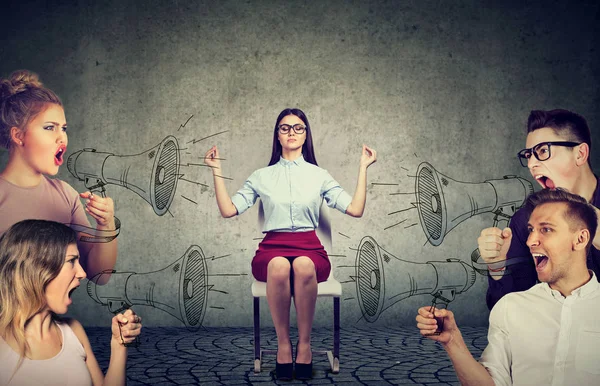 Impassive meditating young businesswoman paying no attention to crowd of screaming in megaphone angry people