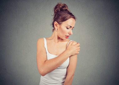 Beyaz kolsuz bluz gri arka plan üzerinde acı ifadesi ile yaralayıcı omuz dokunmadan genç papatyanın kız