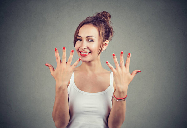 Beautiful happy woman showing hands with trendy red nails looking at camera on gray background