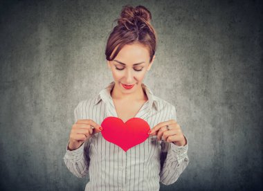 Gömlek gri arka plan üzerinde büyük duygu dolu göğsünde büyük kırmızı kalp tutan güzel kadın