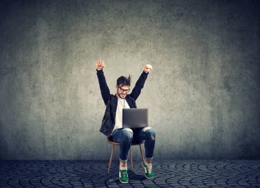 Şık hipster adam iskemlede laptop ve kutlama zafer gri yeni başarı ile heyecan arıyor