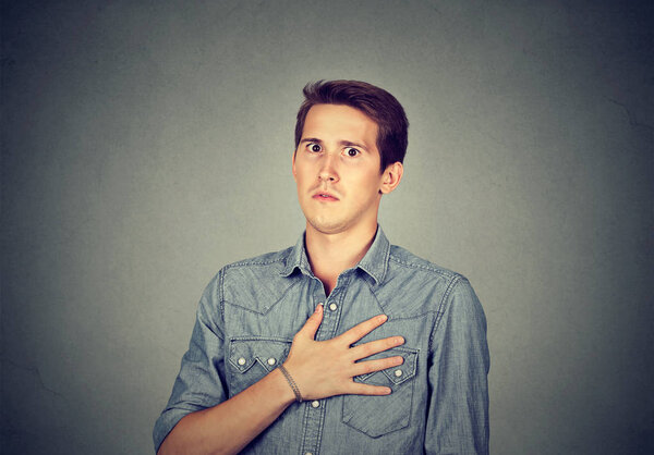 Young man looking super dumbfounded with unbelievable news holding hand on chest and looking stunned at camera