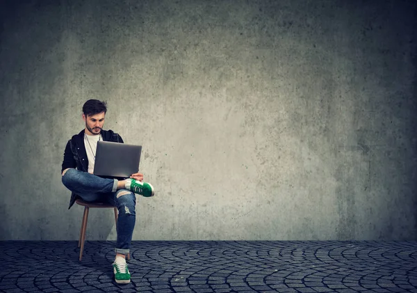 Стильный Молодой Человек Сидящий Стуле Просматривающий Ноутбук Простом Фоне — стоковое фото