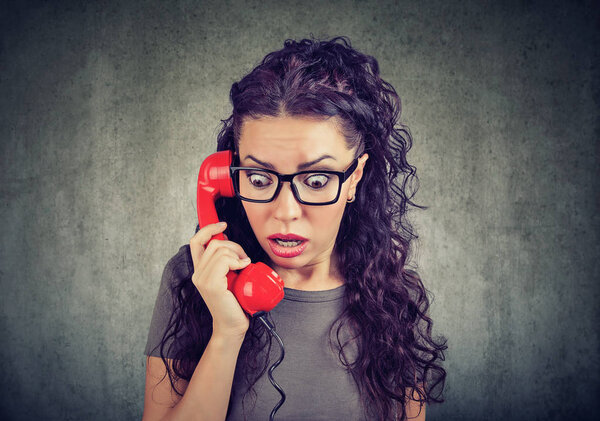 Young brunette in glasses receiving bad news and looking stunned while speaking on phone