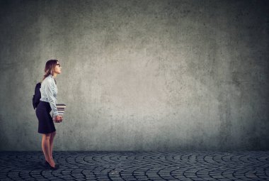 Sırt çantası ve gri arka plan üzerinde kitap yığını holding Gözlük Genç öğrenci yan görünüm